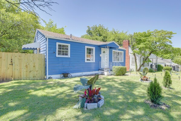 A blue house with a fenced yard, a small garden, and a clear sky.