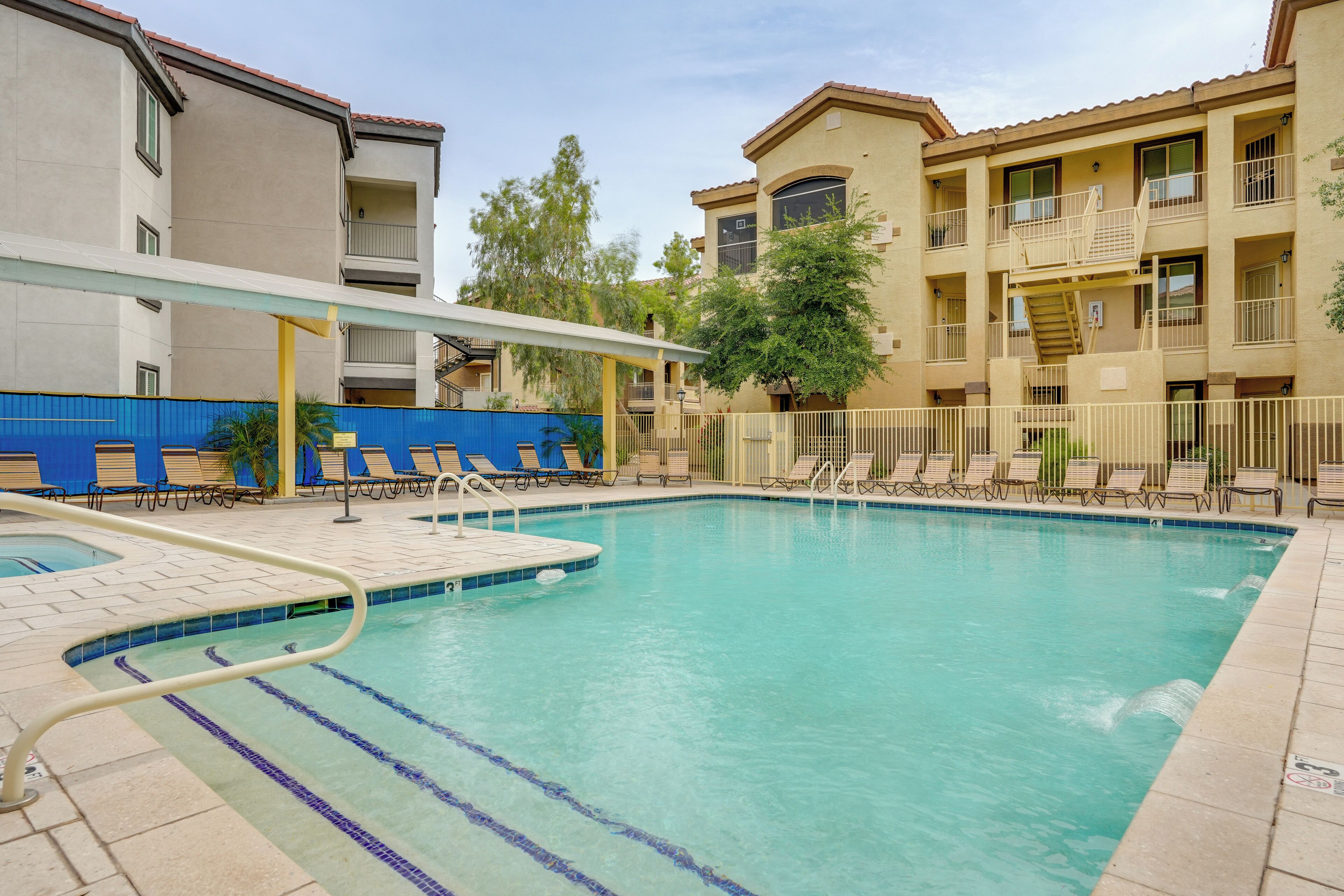 A swimming pool with lounge chairs and a covered area, surrounded by multi-story buildings with balconies.