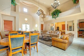 A spacious living room with a dining area, high ceilings, and a kitchen in the background.