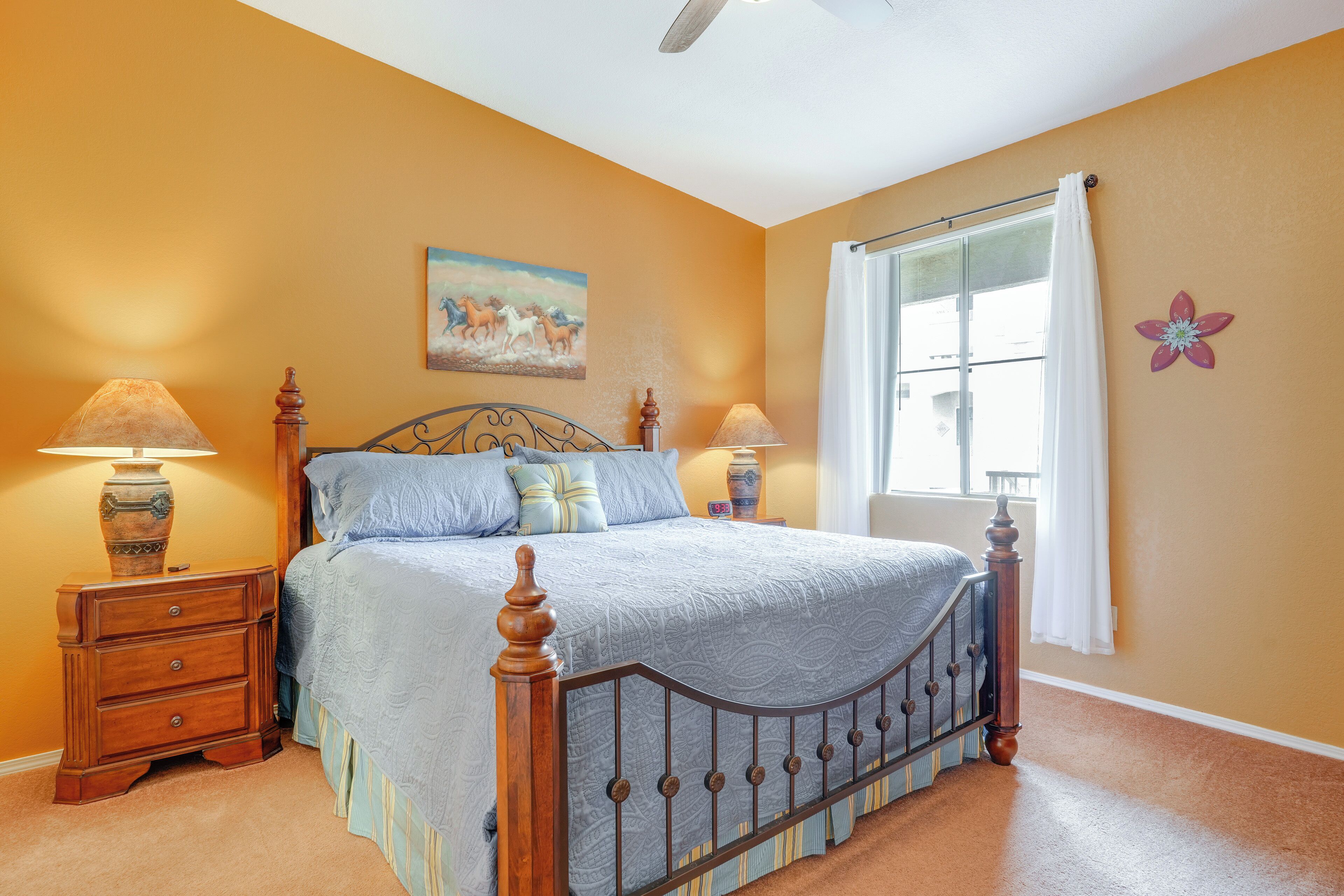 A bedroom with a bed, two nightstands, a window with curtains, and a painting on the wall.