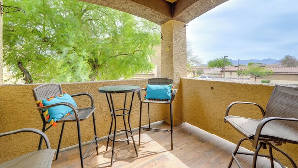 A balcony with wicker chairs and a small table, a view of green trees, and a distant mountain range. - Resort-style Pools & Hot Tubs! Mtn-view Mesa Condo (Mesa)