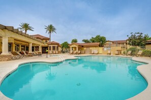 A swimming pool with lounge chairs, palm trees, and a building with a tiled roof.