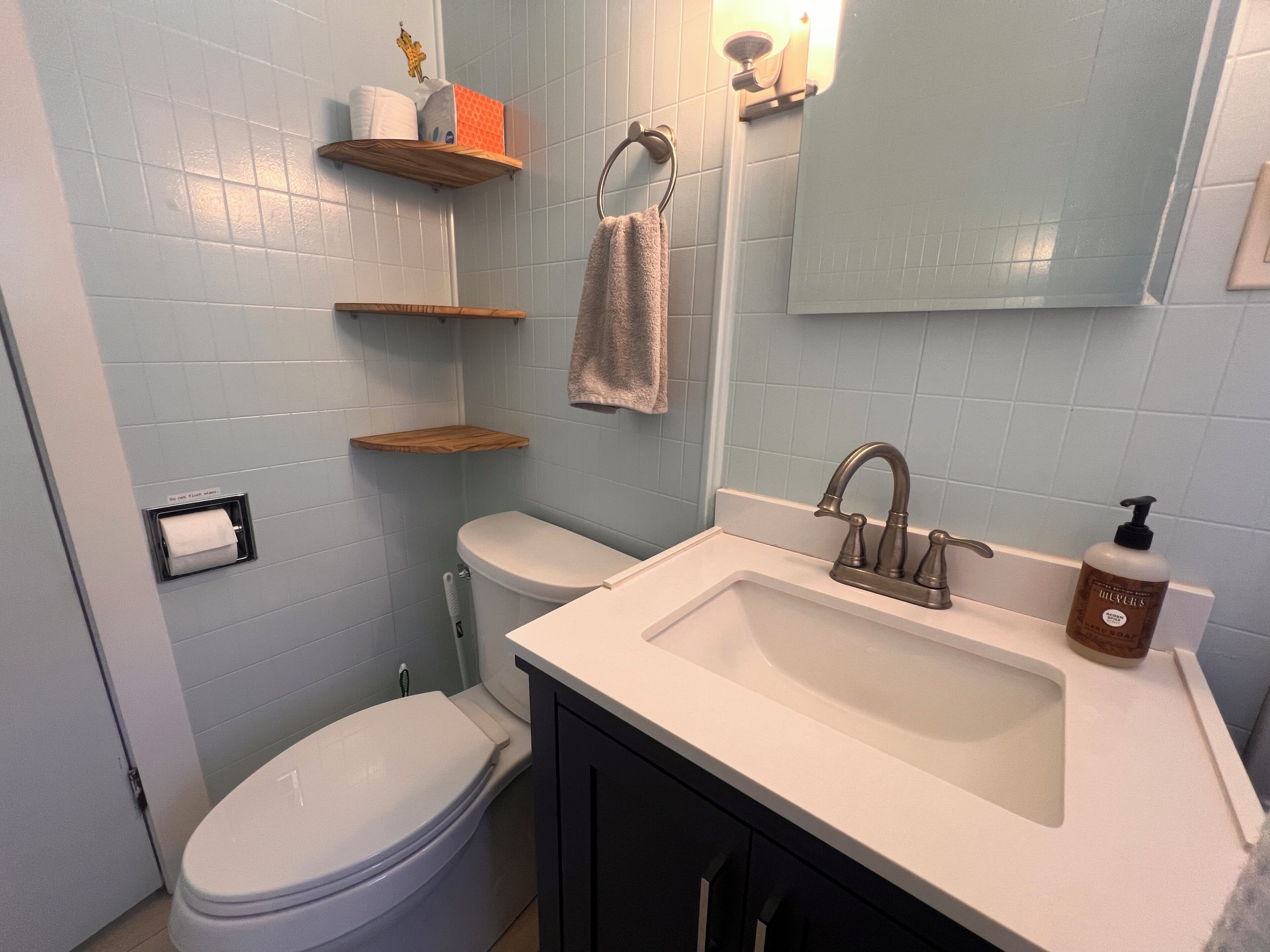Un baño con inodoro, lavamanos y estantes con artículos de aseo.