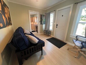 Ein Wohnzimmer mit einem dunkelgrauen Sofa, einer kleinen Holzbank und einer Tür, die in eine Küche führt.