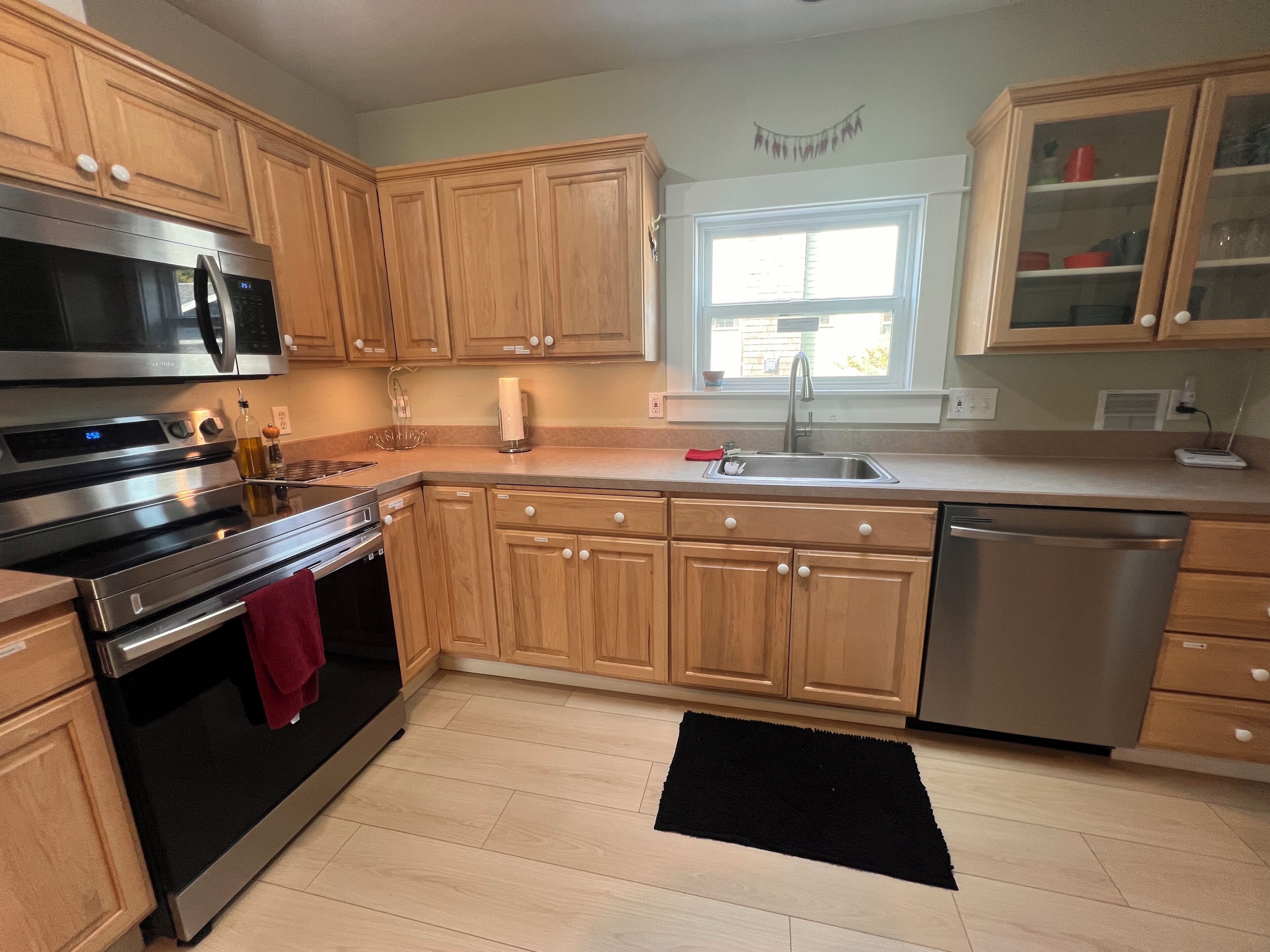 A kitchen with wooden cabinets, stainless steel appliances, a window, and a black rug.