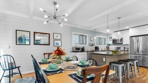 A modern kitchen with a dining area, featuring a central island, bar stools, and a chandelier. - Sand Dollar at Seaside Beach (Seaside)