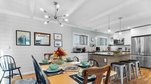 A modern kitchen with a dining area, featuring a central island, bar stools, and a chandelier. - Sand Dollar at Seaside Beach (Seaside)