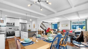 A modern kitchen with stainless steel appliances, a dining area with blue chairs and a wooden table, and a staircase leading to a loft. - Sand Dollar at Seaside Beach (Seaside)