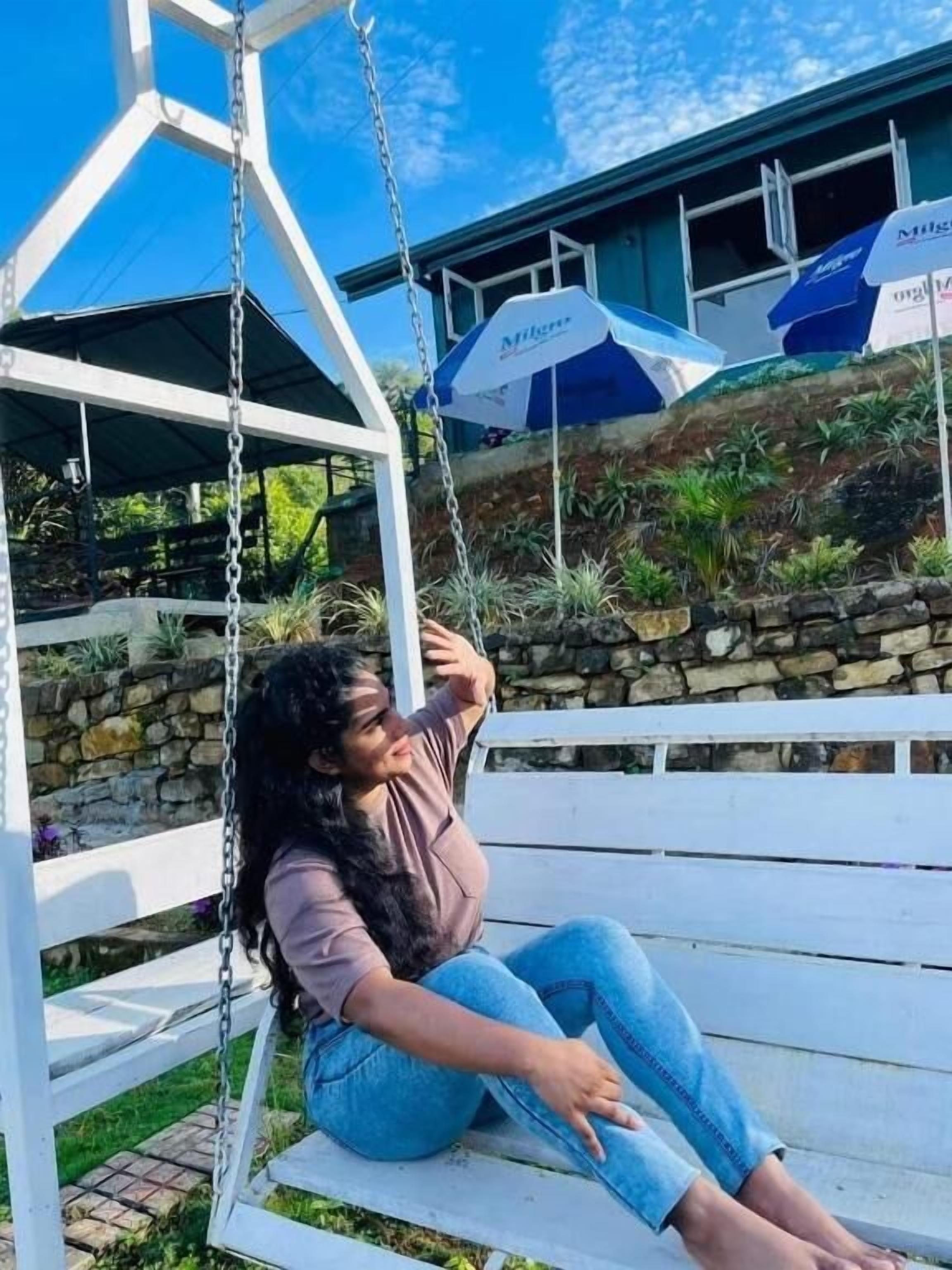 A person sitting on a swing with a stone wall and plants in the background.