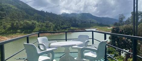 A balcony with a table and chairs, overlooking a river and green hills.