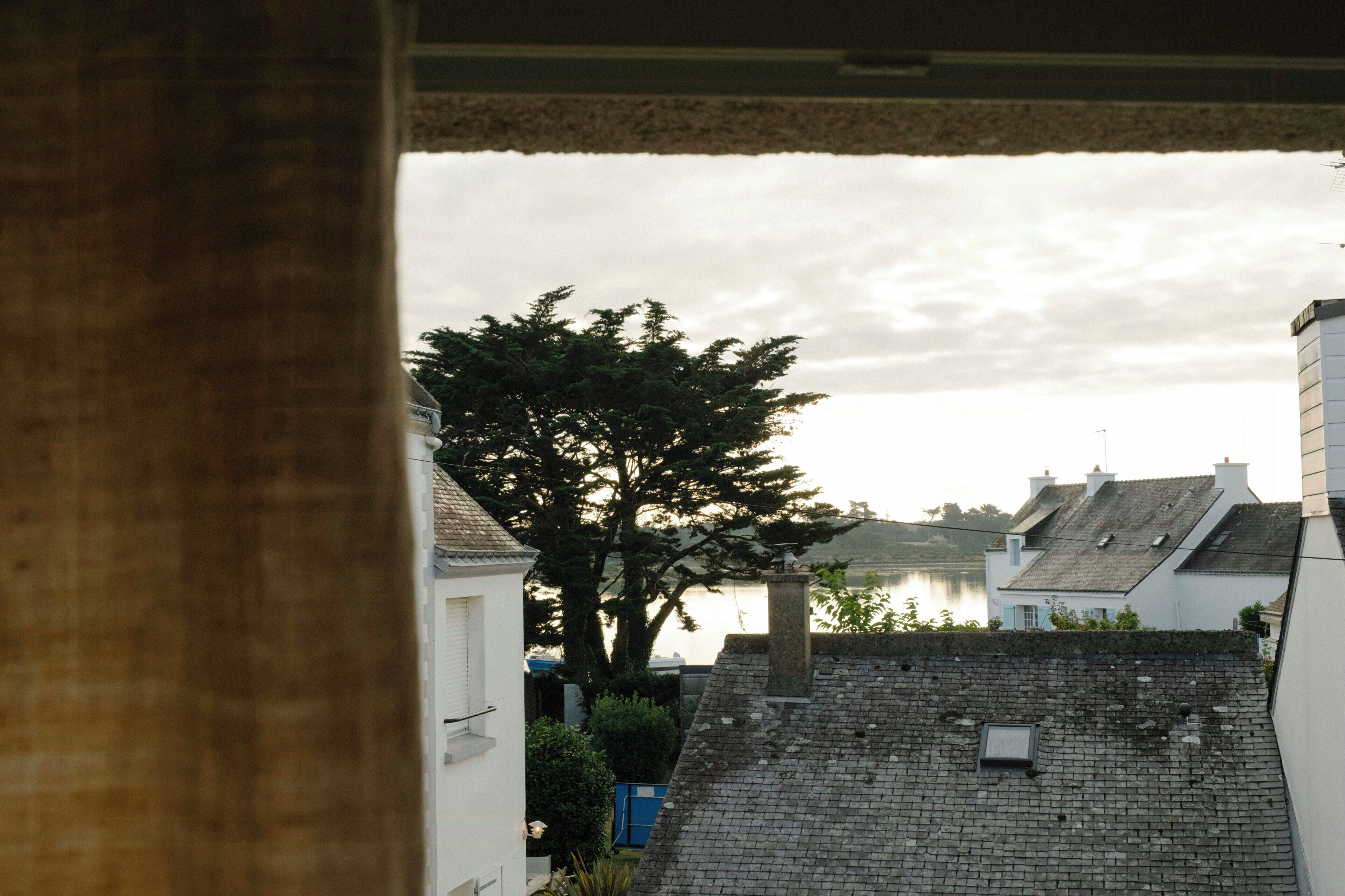 Vista de un edificio con fachada de piedra, un árbol en primer plano y una masa de agua al fondo.