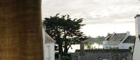 Vista de un edificio con fachada de piedra, un árbol en primer plano y una masa de agua al fondo.