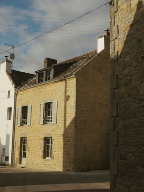 Ein Gebäude aus Stein mit einem geneigten Dach, mehreren Fenstern mit Fensterläden und einer sichtbaren Satellitenschüssel.