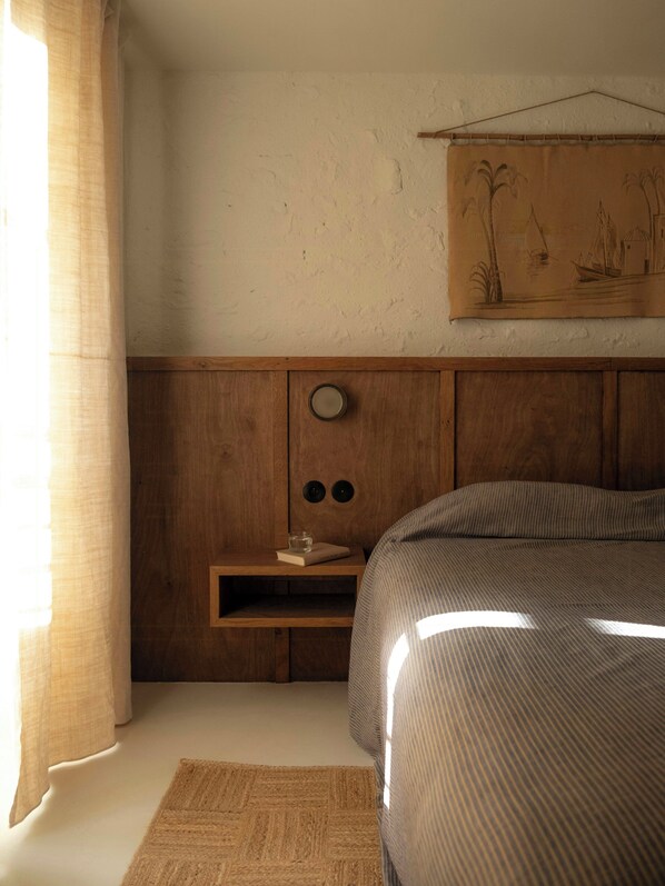 Ein Schlafzimmer mit einem hölzernen Kopfende, einem Nachttisch mit Buch und Glas sowie einem Wandbild.