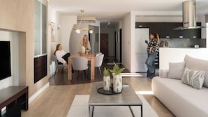 A modern living room with a sofa, coffee table, and a TV. There is a dining area with a table and chairs. A kitchen is visible in the background with cabinets and a stove. - Sopot Haffnera - close to the beach  (Sopot)