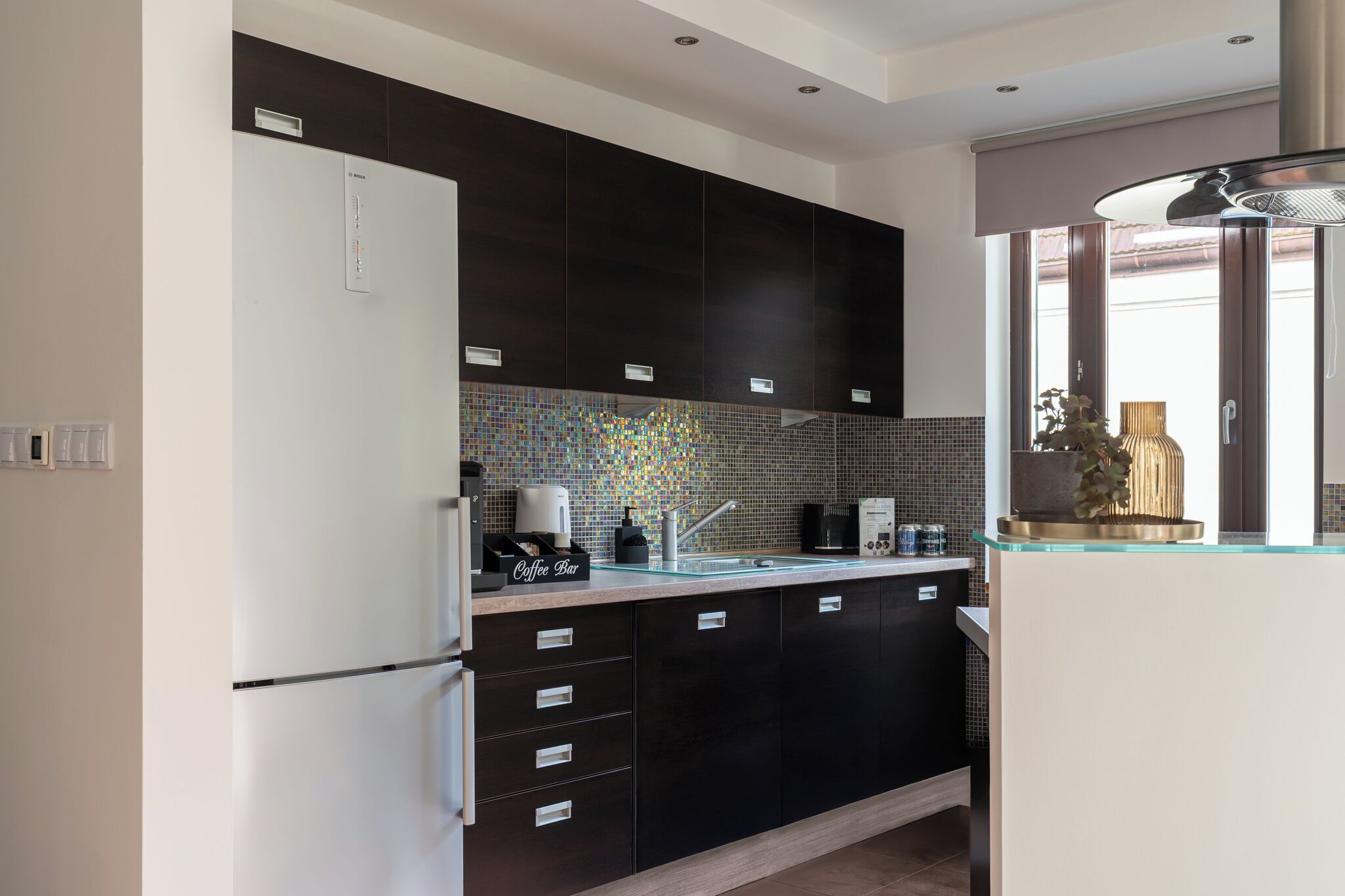 A modern kitchen with dark cabinets, a tiled backsplash, and a coffee bar.