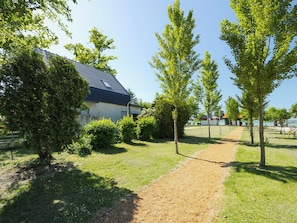 Un bâtiment doté d’un toit en pente, entouré d’un chemin de gravier et d’arbres verdoyants.