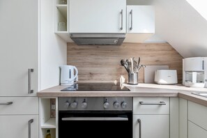 A modern kitchen with white cabinets, a wooden countertop, a built-in oven, and a coffee maker.