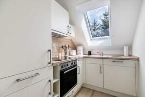 A modern kitchen with white cabinets, a black oven, a skylight, and a window overlooking trees.