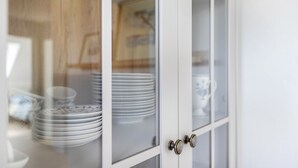 A white cabinet with glass doors, containing stacked white plates and a blue and white patterned bowl. - NEW - Artist’s Retreat Halebüll with Sea View, Shared Terrace and Wi-Fi (Husum)