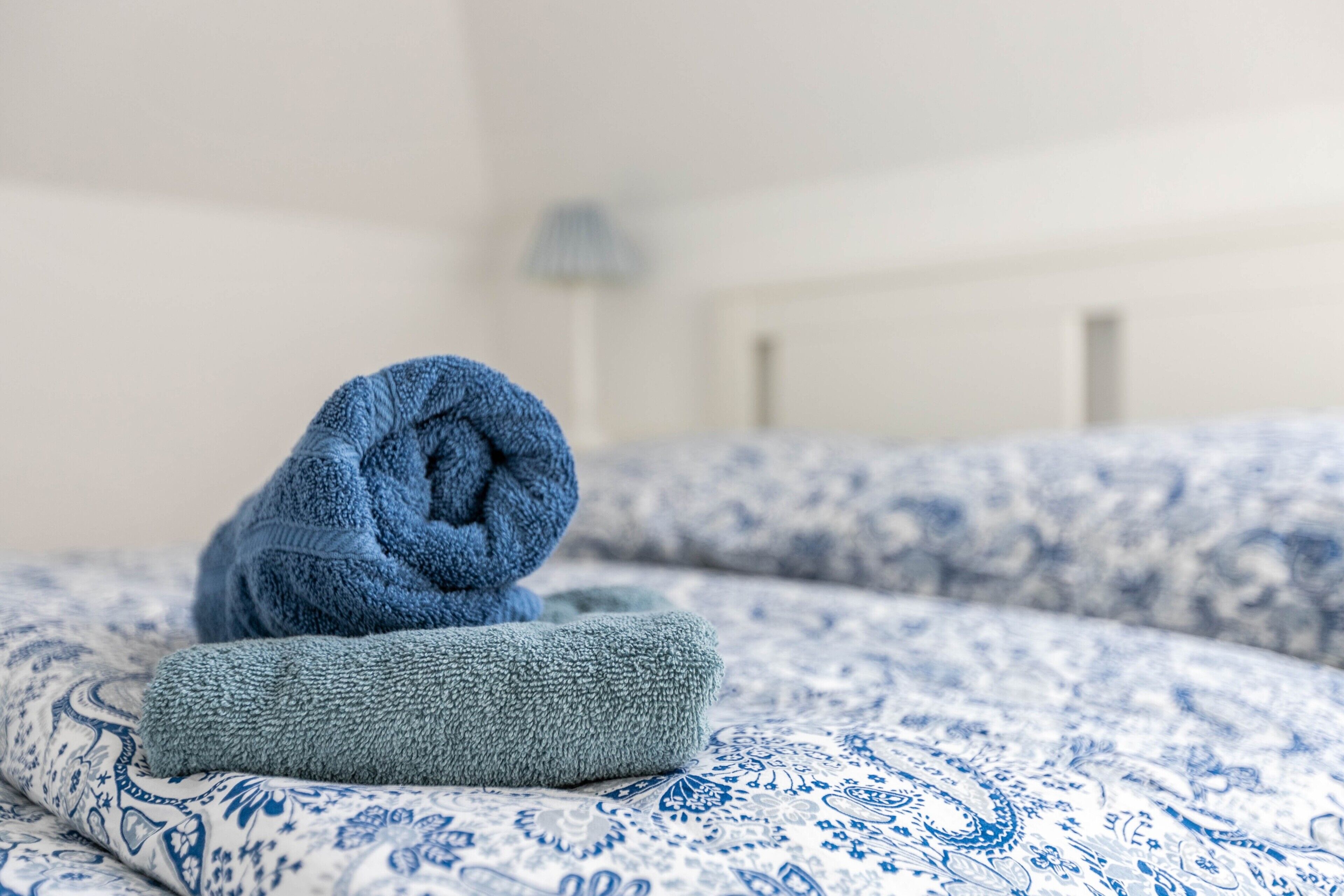 Ein Bett mit einer blau-weißen Tagesdecke und zwei aufgerollten Handtüchern.