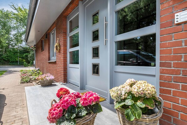 A building with a brick facade, large windows, and a paved entrance area with potted plants.