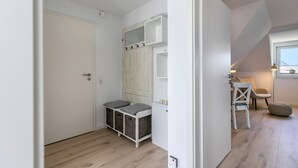 A room with a white door, a wooden wardrobe, a small table with chairs, and a window. - Modern Coastal Retreat – Newly Renovated with Partial Sea View, Shared Garden & Wi-Fi (Husum)