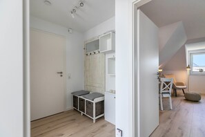 A room with a white door, a wooden wardrobe, a small table with chairs, and a window.