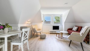 A modern loft bedroom with a sloped ceiling, a large window, a flat-screen TV, and a cozy seating area with a sofa and chairs. - Modern Coastal Retreat – Newly Renovated with Partial Sea View, Shared Garden & Wi-Fi (Husum)