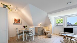 A modern interior with a dining area, a sofa, a TV, and a window with a view. - Modern Coastal Retreat – Newly Renovated with Partial Sea View, Shared Garden & Wi-Fi (Husum)
