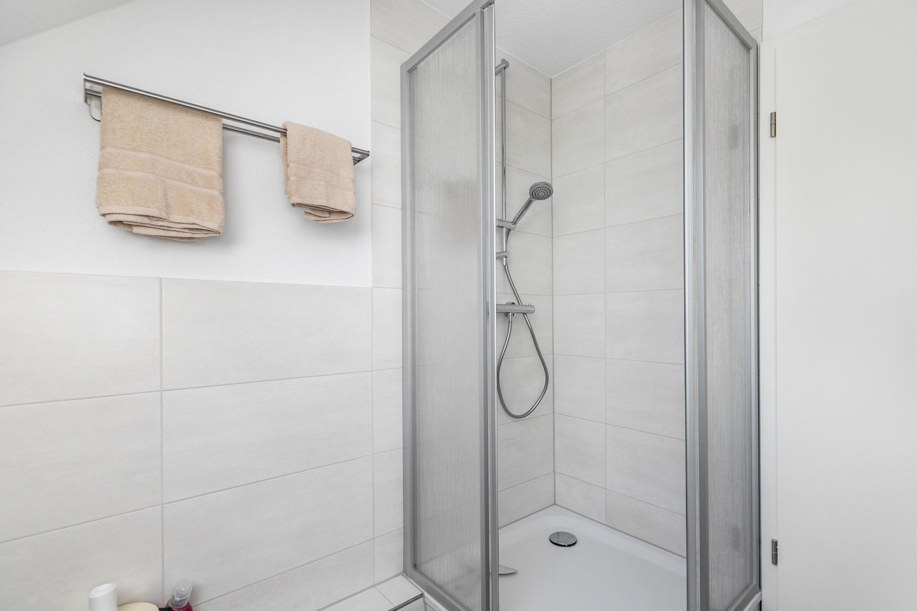 Une salle de bain moderne avec une douche à parois de verre, des carreaux blancs et deux serviettes posées sur un porte-serviettes.