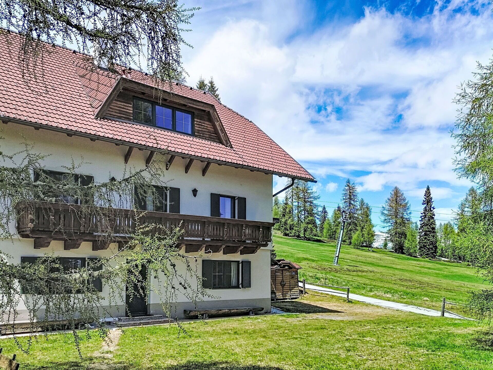 Een chalet met twee verdiepingen, een rode pannendak, houten balkon en een gazon.