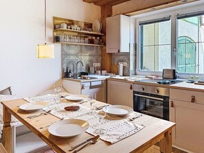Eine Küche mit Esstisch, gedeckt für vier Personen, einem eingebauten Backofen und einem Fenster mit Blick ins Freie.