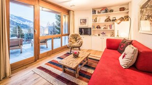 Een gezellige woonkamer met een rode bank, een houten salontafel en uitzicht op een besneeuwde berg door grote glazen deuren.