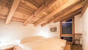 Een slaapkamer met een houten plafond, een bed, een raam en een stoel.