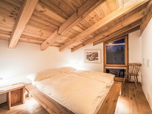 Ein Schlafzimmer mit Holzbalkendecke, einem Bett, einem Fenster und einem Stuhl.
