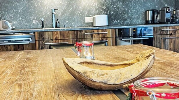 Een houten eettafel met een kaars en een glazen pot in het midden.