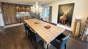 Een moderne keuken met houten kastjes, een eettafel met stoelen, een kroonluchter en een schilderij van een hert op de muur.