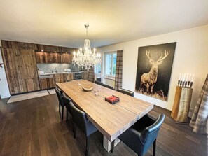 A modern kitchen with wooden cabinets, a dining table with chairs, a chandelier, and a deer painting on the wall.