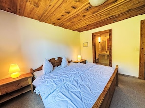 Une chambre à coucher avec un plafond en bois, un lit recouvert d’une couette bleue, deux lampes de chevet et une table de chevet en bois.