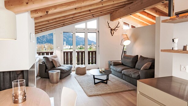 Un soggiorno moderno con soffitto in legno, un divano, un tavolino da caffè e vista sulle montagne.