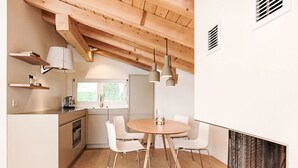 Una cucina moderna con zona pranzo, travi in legno a soffitto, mobili bianchi e illuminazione a sospensione.