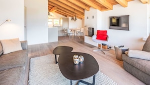Un soggiorno moderno con soffitto in legno, un tavolino da caffè nero con candele, un divano grigio e una poltrona rossa.
