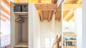 Un interno moderno con soffitto in legno, un armadio a muro con spazio per appendere e una libreria, oltre a una scala.