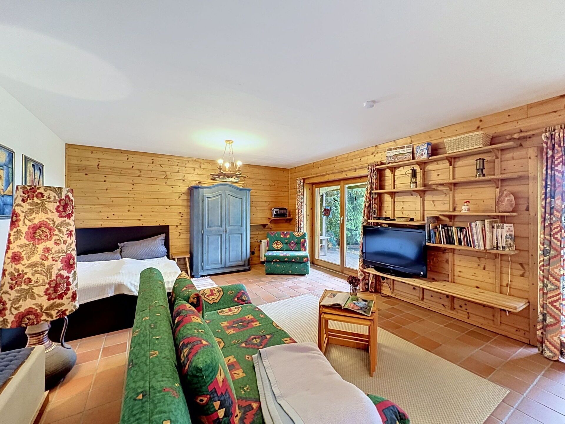 Ein Zimmer mit Holzwänden, einem Bett, einem Sofa, einem Fernseher und Regalen mit Büchern und Dekoration.