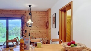 Un intérieur en bois comprenant une table à manger, des chaises, un luminaire suspendu et une vue par une fenêtre.