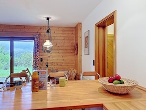 Ein Holzinnenraum mit Esstisch, Stühlen, einer Hängelampe und Blick durch ein Fenster.
