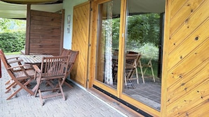 Une cabane en bois dotée d’un patio couvert, d’une table à manger avec des chaises et d’une porte-fenêtre coulissante donnant sur un espace extérieur.