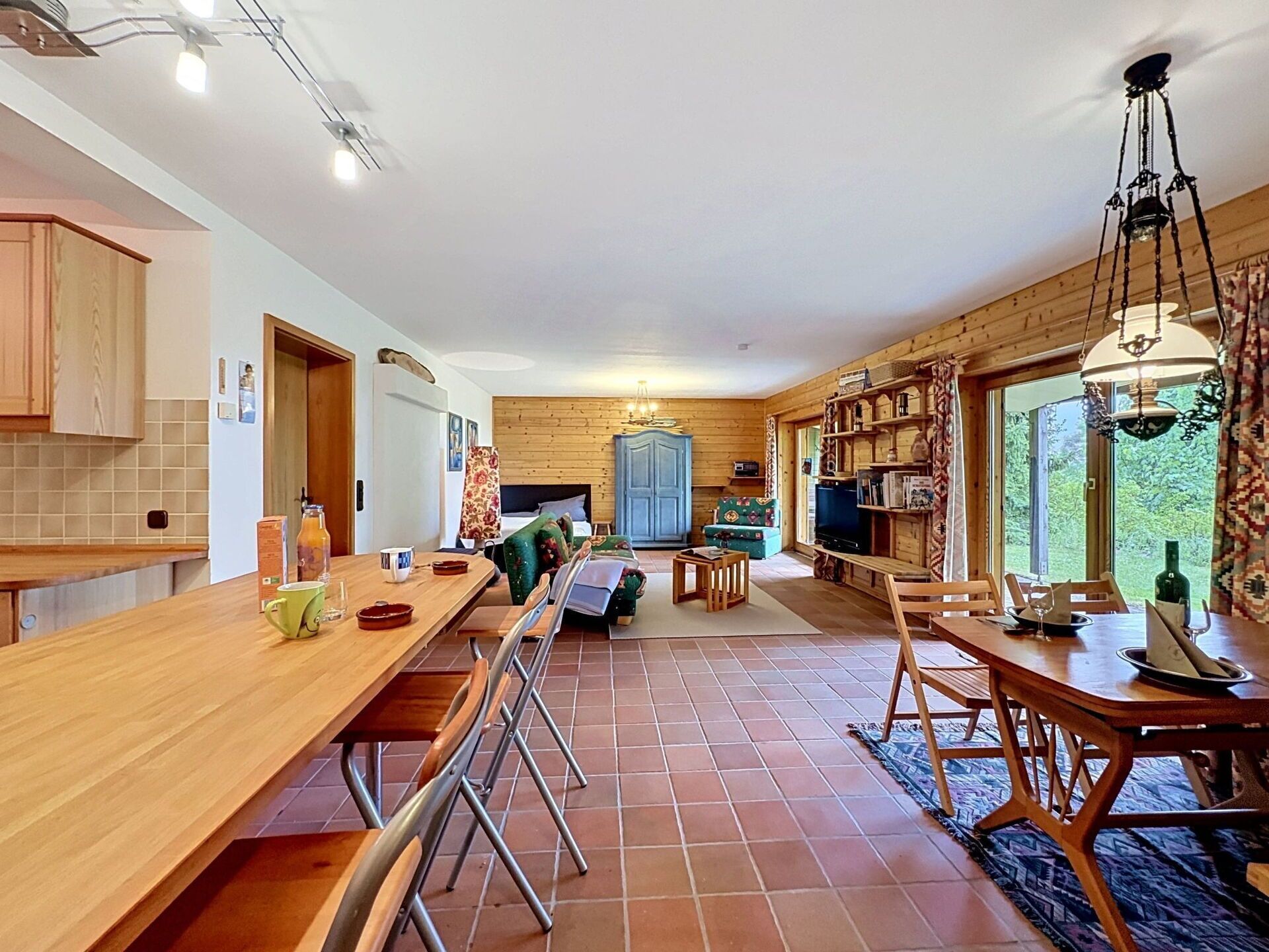 Une cuisine spacieuse avec une longue table en bois, un coin repas avec des chaises, un canapé et un téléviseur.