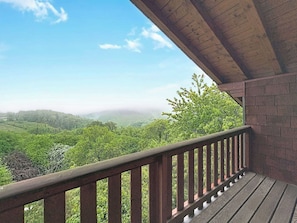 Ein Balkon mit Holzgeländer, der auf eine üppige, grüne Landschaft blickt.